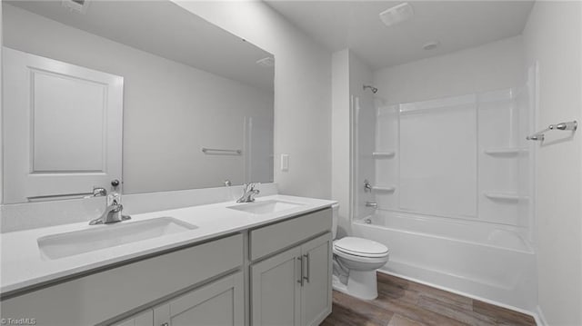 bathroom featuring double vanity, wood finished floors, toilet, and a sink