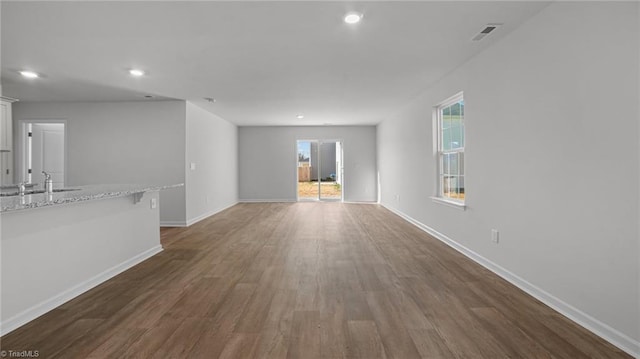 unfurnished living room with visible vents, baseboards, recessed lighting, wood finished floors, and a sink