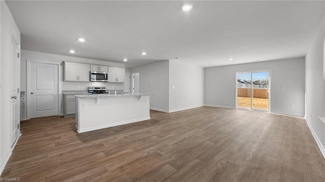 kitchen with dark wood-type flooring, a kitchen island with sink, open floor plan, recessed lighting, and appliances with stainless steel finishes