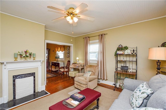 living room with baseboards, ornamental molding, a fireplace, wood finished floors, and a ceiling fan