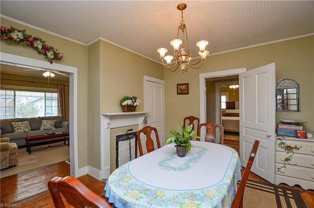 dining space featuring a notable chandelier, wood finished floors, a fireplace, crown molding, and baseboards