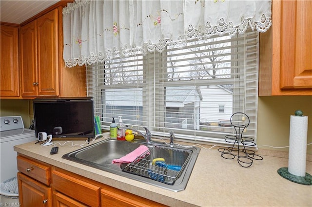 kitchen featuring washer / dryer, brown cabinetry, light countertops, and a sink