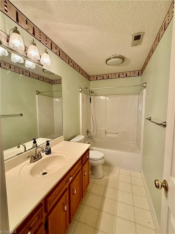 full bathroom with vanity, shower / bath combination, a textured ceiling, and toilet