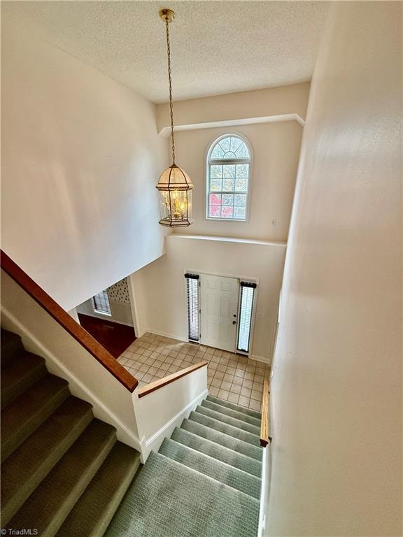 staircase featuring tile patterned flooring, a notable chandelier, and a textured ceiling