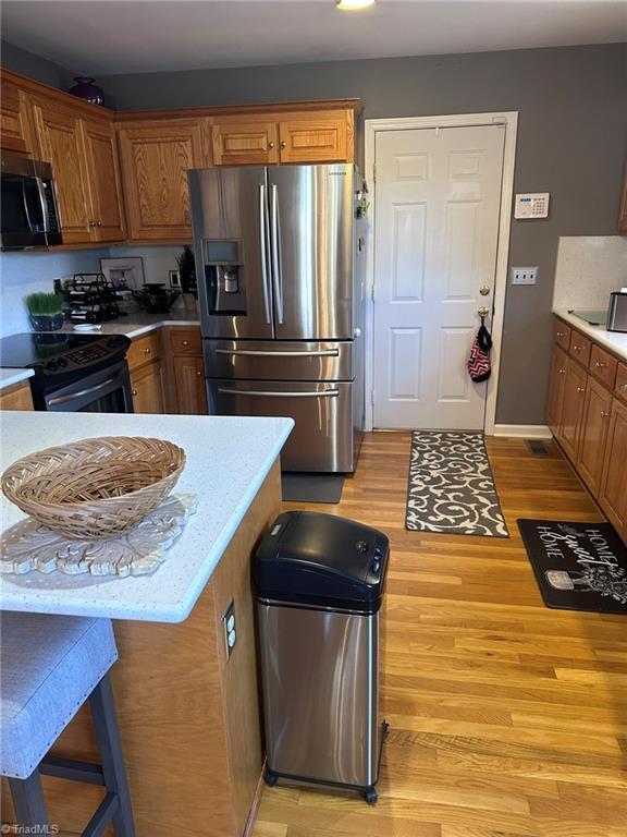 kitchen featuring a breakfast bar area, black range with electric stovetop, light hardwood / wood-style floors, and stainless steel refrigerator with ice dispenser