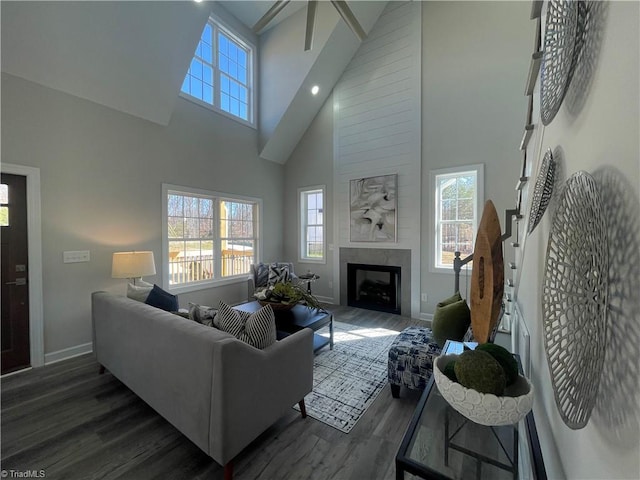 living room featuring high vaulted ceiling, wood finished floors, baseboards, and a large fireplace