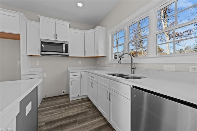 kitchen featuring light stone countertops, a sink, dark wood-type flooring, appliances with stainless steel finishes, and white cabinetry