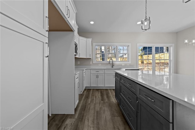 kitchen with stainless steel microwave, hanging light fixtures, dark wood-style floors, white cabinetry, and a sink