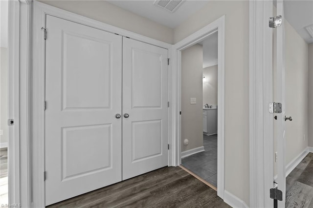 corridor featuring visible vents, a sink, baseboards, and dark wood-style flooring