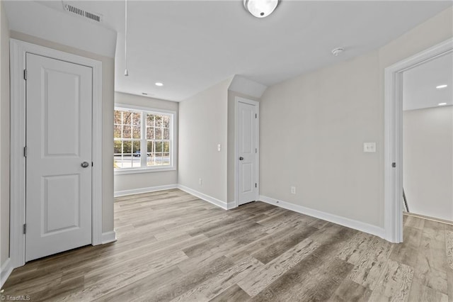 empty room with attic access, light wood-style floors, visible vents, and baseboards