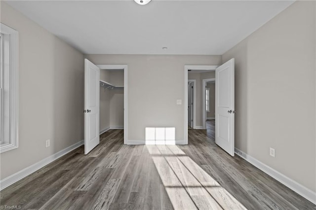 unfurnished bedroom with a closet, baseboards, wood finished floors, and a spacious closet