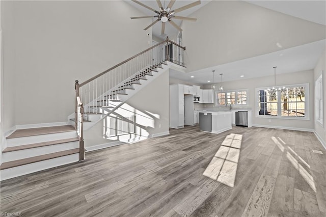 unfurnished living room featuring stairway, light wood-style flooring, baseboards, and a sink