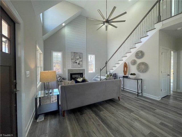 living area featuring baseboards, high vaulted ceiling, stairs, dark wood-type flooring, and a large fireplace