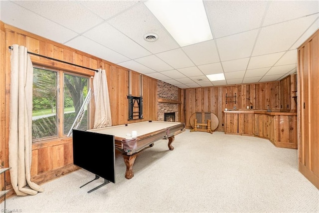 playroom featuring wooden walls, a fireplace, pool table, light colored carpet, and a paneled ceiling