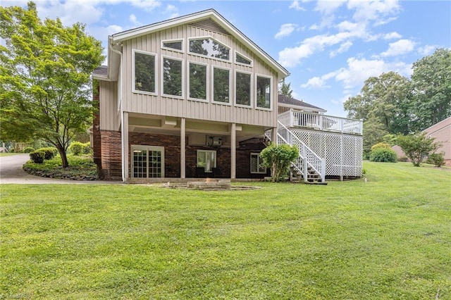 rear view of property featuring stairs, a lawn, a deck, and brick siding