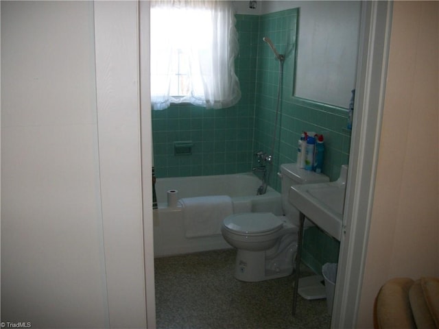 bathroom with tile walls, toilet, and tiled shower / bath