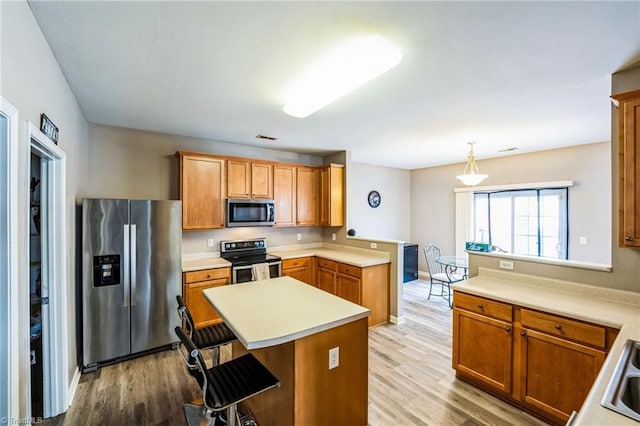 kitchen featuring decorative light fixtures, appliances with stainless steel finishes, a kitchen breakfast bar, kitchen peninsula, and light hardwood / wood-style floors