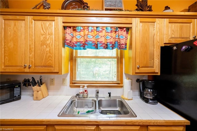 kitchen featuring black appliances, tile countertops, tasteful backsplash, and sink