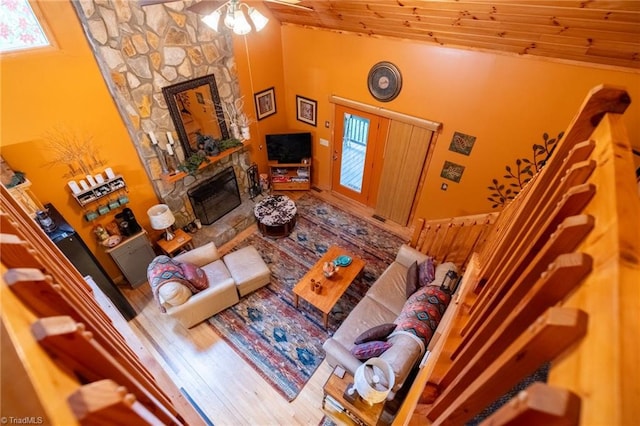 living room featuring wood ceiling, ceiling fan, hardwood / wood-style flooring, and a stone fireplace