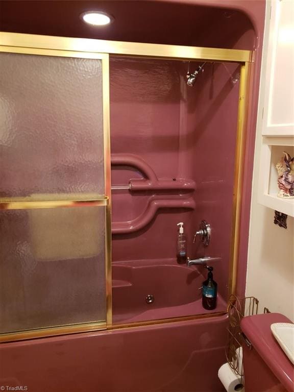 bathroom featuring toilet and bath / shower combo with glass door