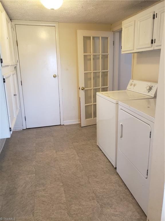 clothes washing area with cabinets, a textured ceiling, and washing machine and dryer