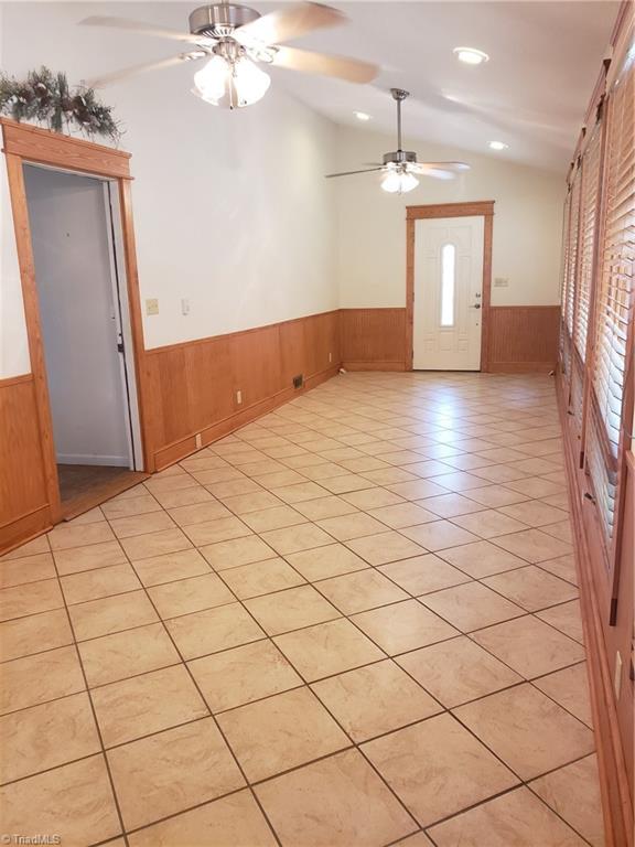 tiled entrance foyer with vaulted ceiling, ceiling fan, and wood walls