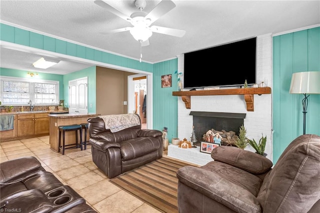 tiled living room with ceiling fan, sink, crown molding, a textured ceiling, and a fireplace