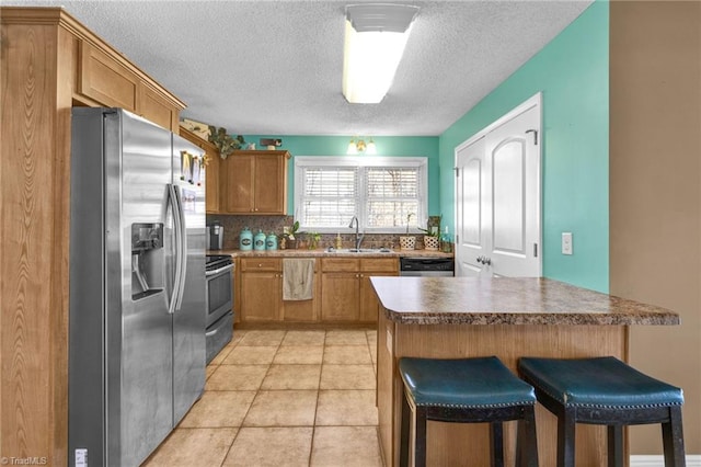 kitchen with appliances with stainless steel finishes, a kitchen breakfast bar, a textured ceiling, sink, and light tile patterned flooring