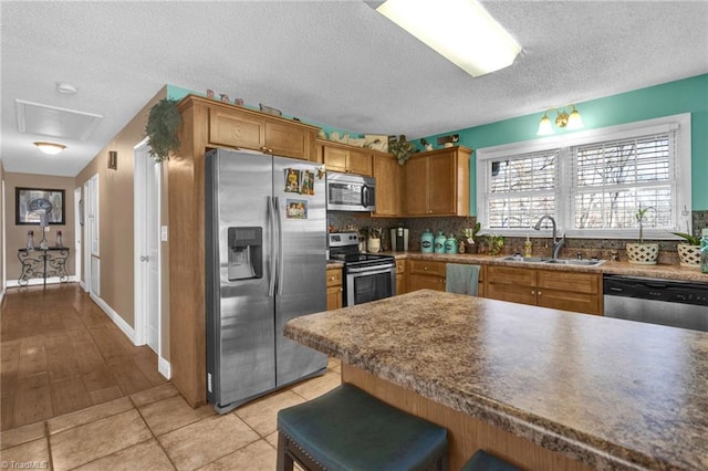 kitchen with decorative backsplash, appliances with stainless steel finishes, a breakfast bar, a textured ceiling, and sink