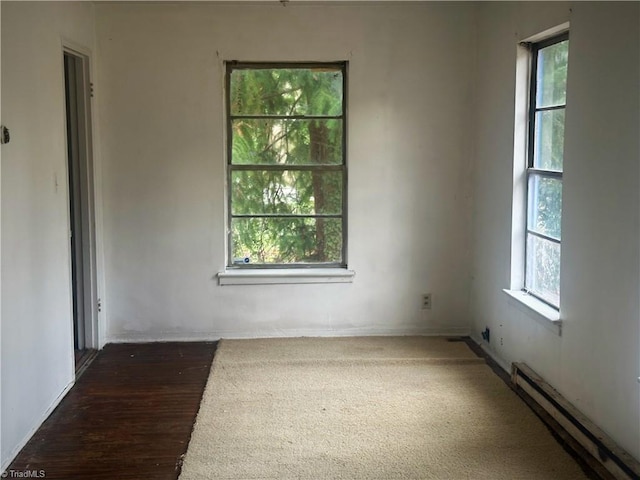 empty room featuring a baseboard heating unit, wood finished floors, a healthy amount of sunlight, and baseboards