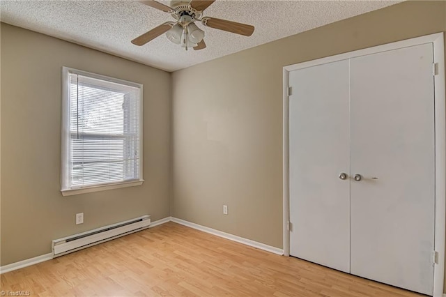 unfurnished bedroom with ceiling fan, baseboard heating, light hardwood / wood-style flooring, a textured ceiling, and a closet