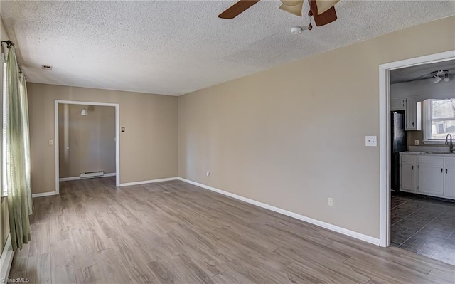 spare room featuring a baseboard heating unit, sink, light hardwood / wood-style flooring, ceiling fan, and a textured ceiling