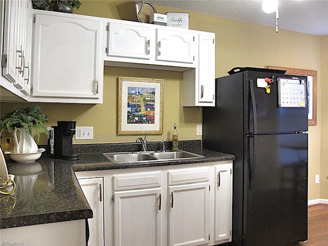 kitchen featuring dark countertops, white cabinets, freestanding refrigerator, and a sink