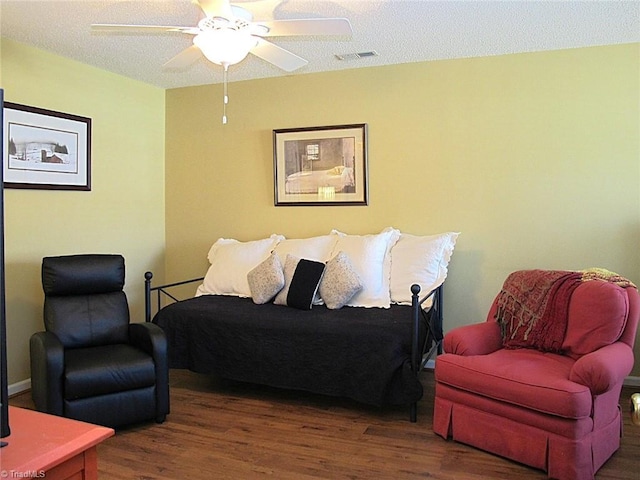 living room with a textured ceiling, wood finished floors, visible vents, and ceiling fan