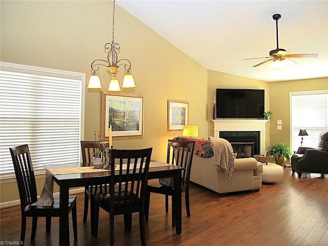 dining area featuring dark wood-style floors, ceiling fan with notable chandelier, a fireplace, and high vaulted ceiling