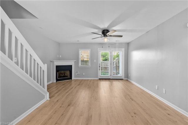 unfurnished living room featuring light wood-style floors, baseboards, ceiling fan, and a fireplace