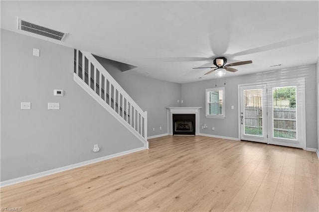 unfurnished living room featuring ceiling fan, light wood-style floors, stairs, baseboards, and visible vents
