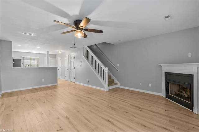 unfurnished living room with light wood-type flooring, a ceiling fan, stairs, and a fireplace