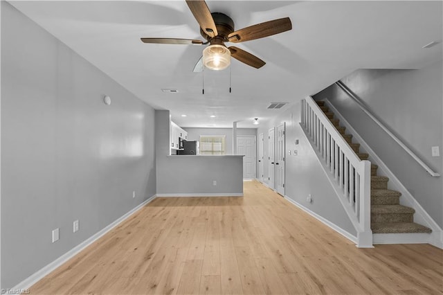 unfurnished living room featuring ceiling fan, visible vents, baseboards, light wood finished floors, and stairs