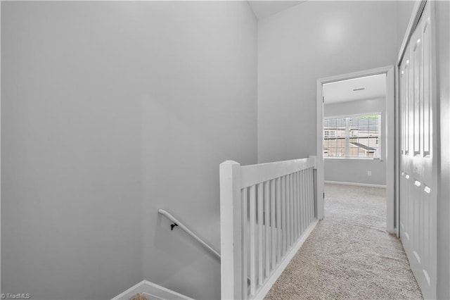 hall featuring carpet floors, baseboards, and an upstairs landing