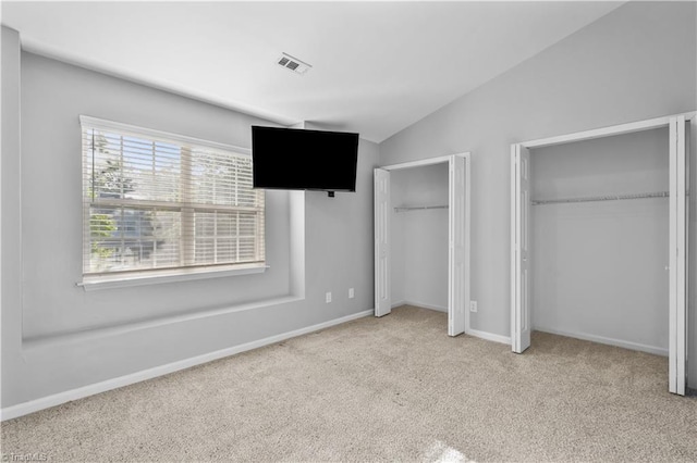 unfurnished bedroom with visible vents, lofted ceiling, two closets, baseboards, and carpet flooring