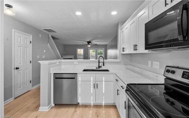kitchen featuring ceiling fan, appliances with stainless steel finishes, light stone countertops, a sink, and light wood finished floors