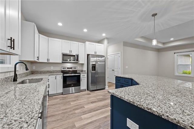 kitchen with stainless steel appliances, a sink, light wood-type flooring, white cabinetry, and light stone counters