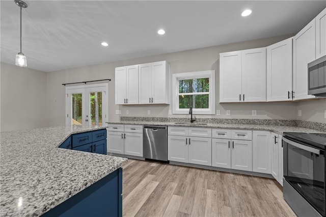 kitchen featuring appliances with stainless steel finishes, a sink, white cabinets, light wood finished floors, and light stone counters