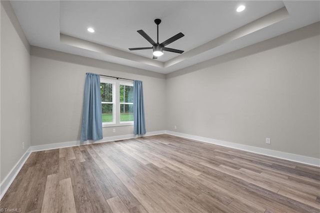 unfurnished room featuring a tray ceiling, wood finished floors, ceiling fan, baseboards, and recessed lighting