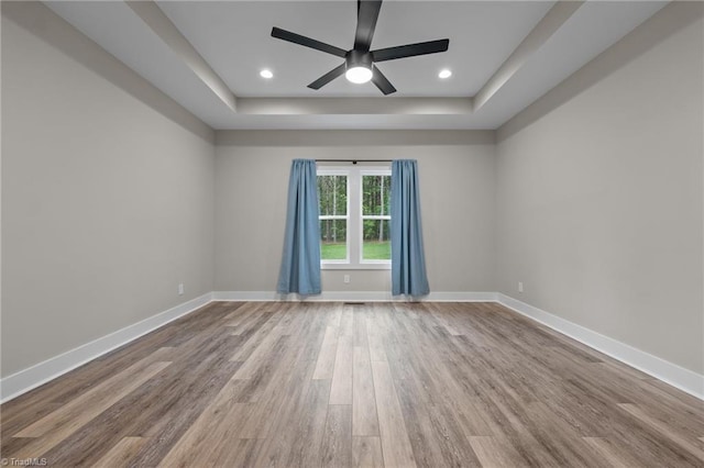 unfurnished room featuring a tray ceiling, wood finished floors, a ceiling fan, baseboards, and recessed lighting