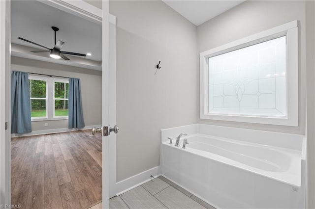 full bathroom with a garden tub, wood finished floors, ceiling fan, and baseboards