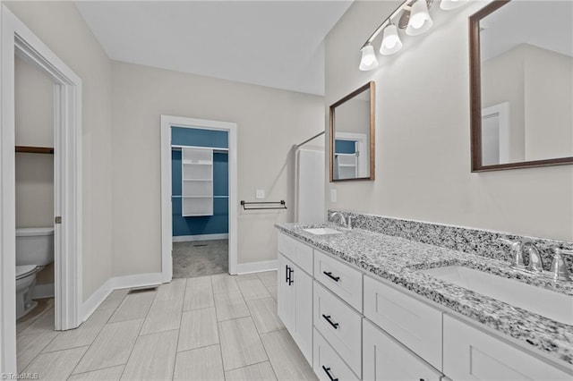bathroom with toilet, a walk in closet, baseboards, and double vanity