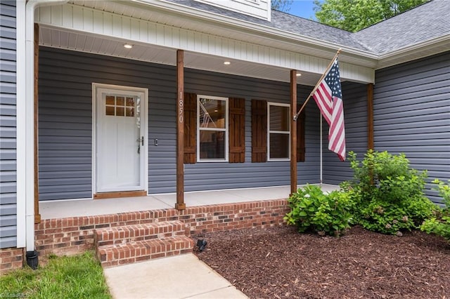 entrance to property with a porch and a shingled roof