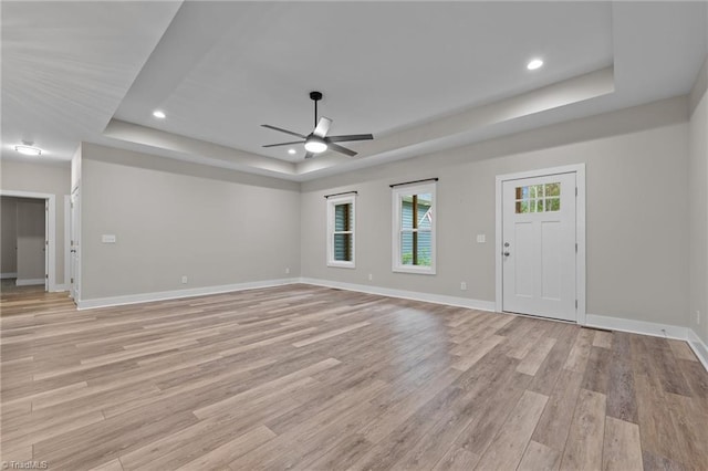 unfurnished living room with a tray ceiling, a ceiling fan, light wood-type flooring, baseboards, and recessed lighting